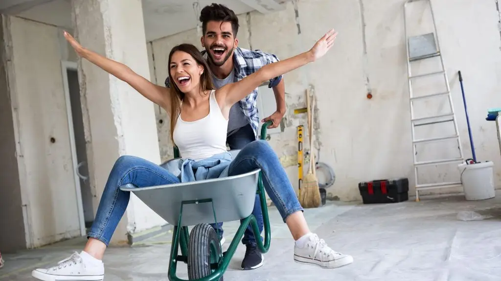 Couple laughs as husband pushes wife in a wheelbarrow