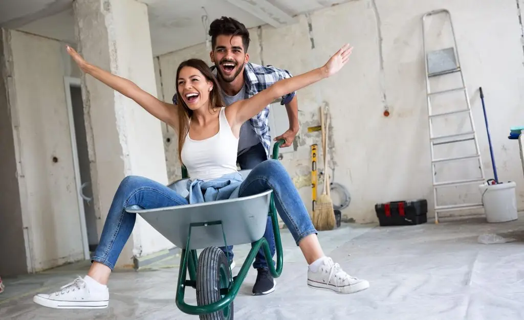 husband enjoying life with wife while pushing her in a wheelbarrow in a house under construction